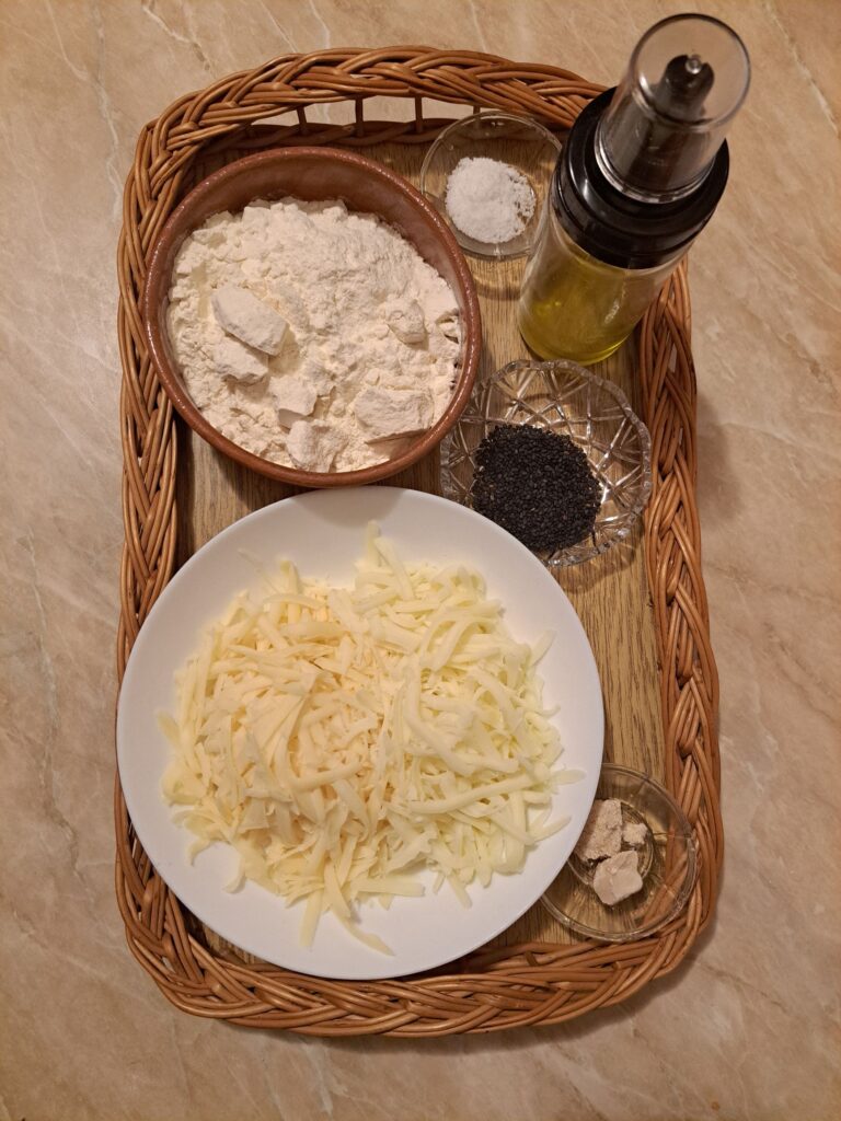 Flour, fresh yeast, grated Kashkaval and mozzarella, salt, black sesame, and oil arranged on a kitchen table for making a Cheese Microgreens Stuffed Sandwich.
