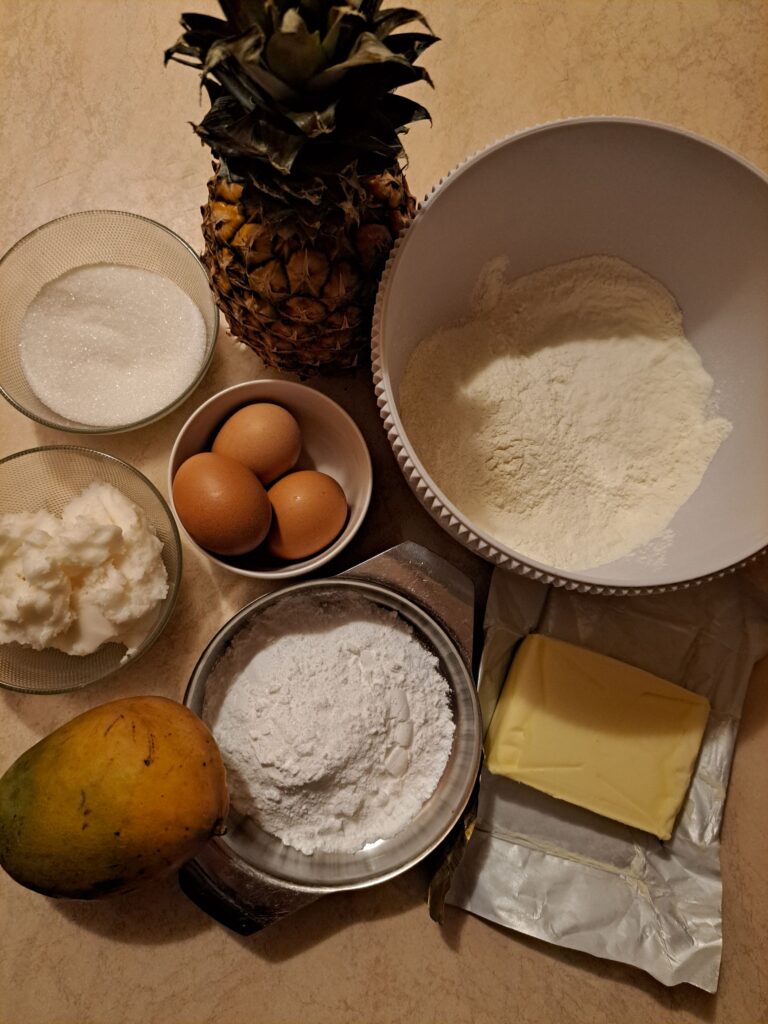 Ingredients for Baked Pineapple Mango Tart neatly arranged on a kitchen counter, including flour, eggs, sugar, butter, pineapple, and mango.