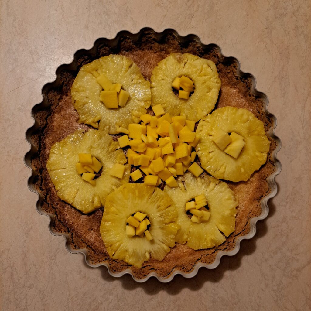 Baked Pineapple Mango Tart shown finished in a tart pan with pineapple rings and mango pieces on top.