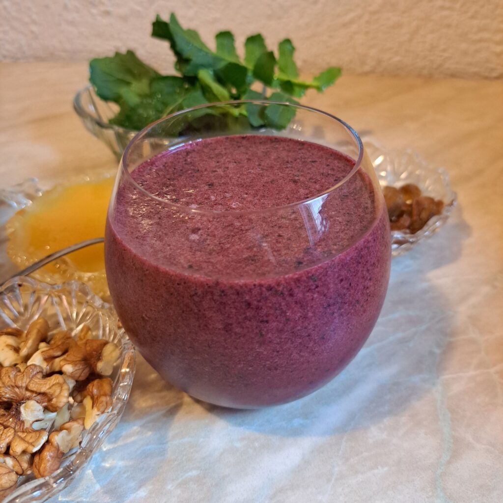 Glass of Berry Arugula Walnut Juice served in a low round glass on a table.