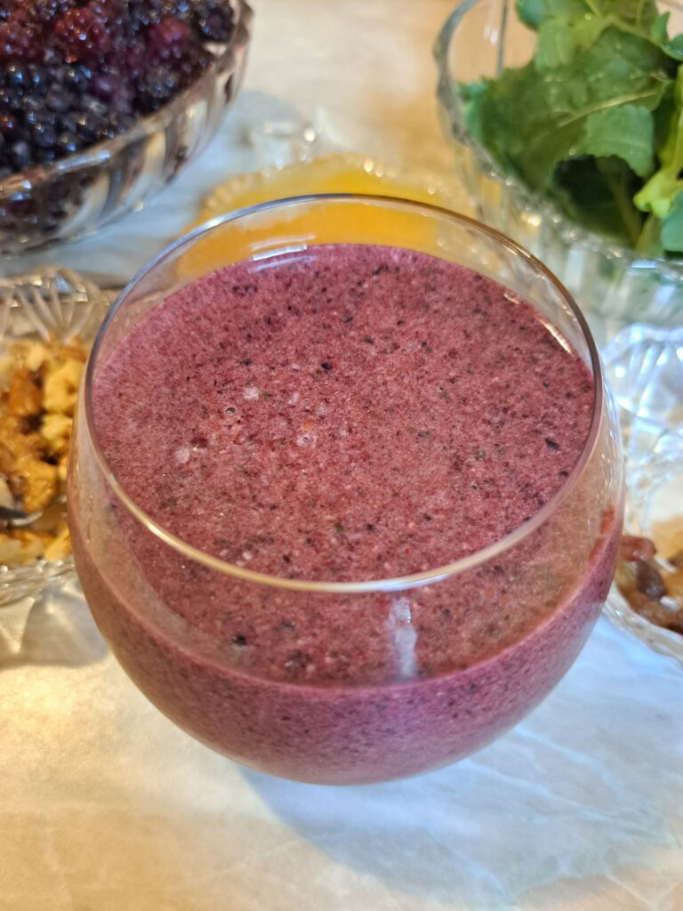 Glass of Berry Arugula Walnut Juice on a table with all ingredients in the background.