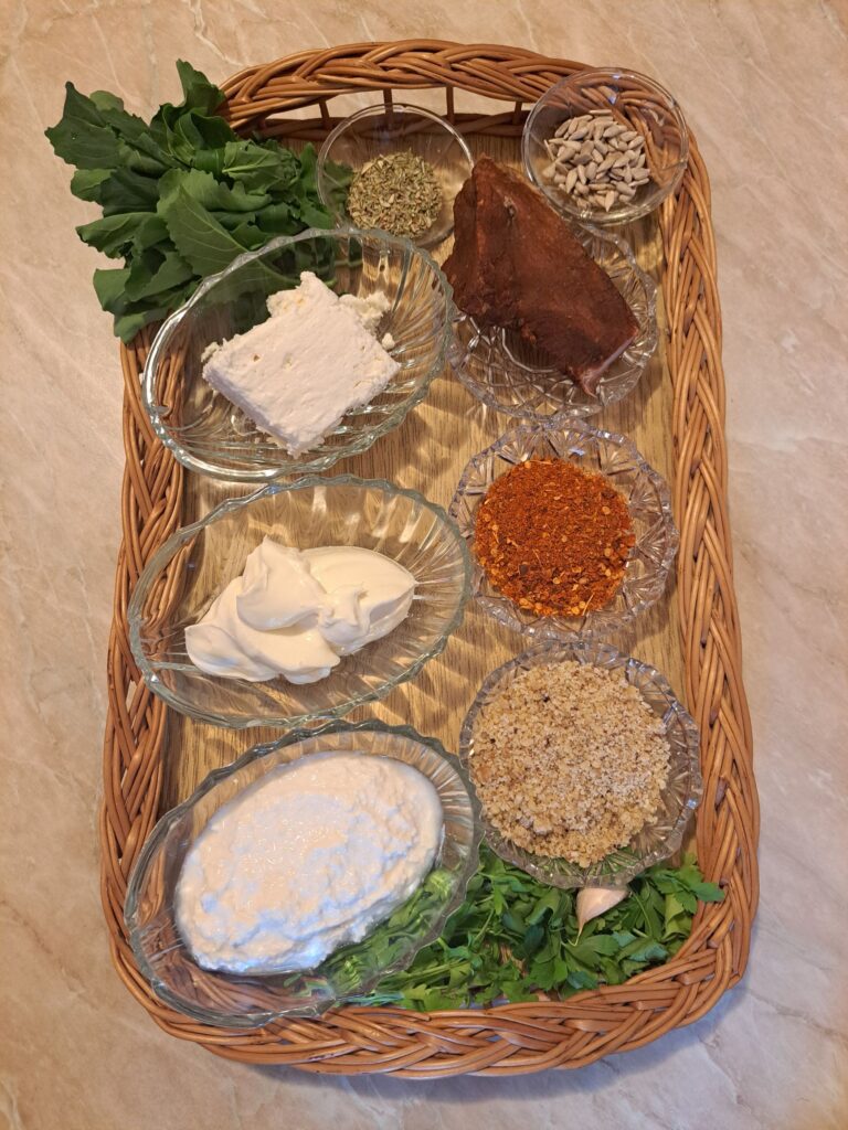Hard cheese, ricotta, cream cheese, roasted sunflower seeds, cured pork meat, garlic, oregano, and coatings arranged on a wooden serving board.
