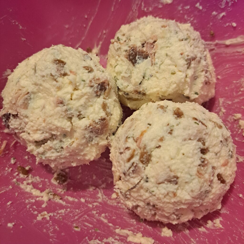 Three formed cheese balls made from mixed cheeses, cured pork meat, and sunflower seeds, shown before coating.