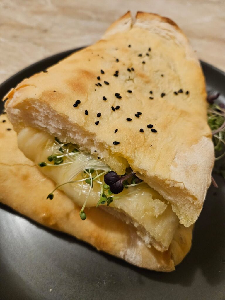 Cheese microgreens stuffed sandwich cut into two halves and served on a plate.