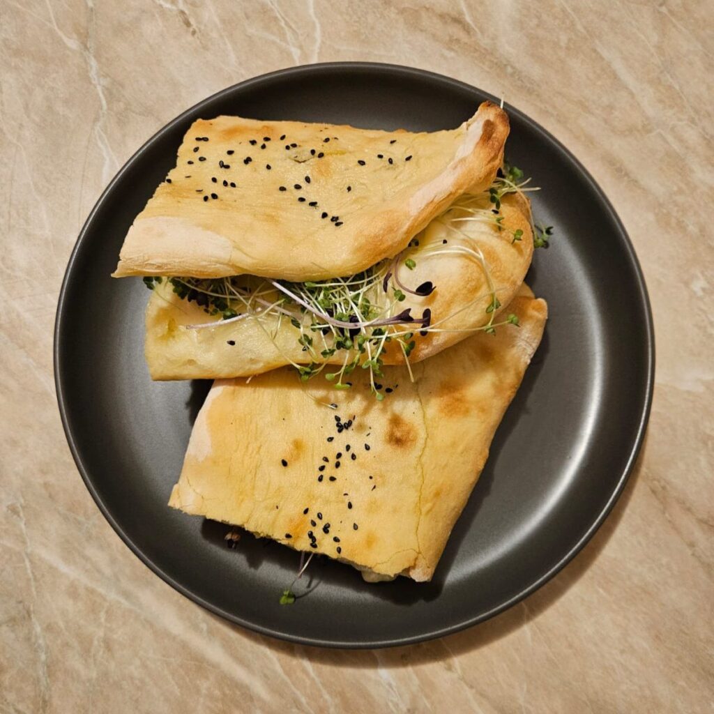Cheese microgreens stuffed sandwich served on a plate, cut into two halves.