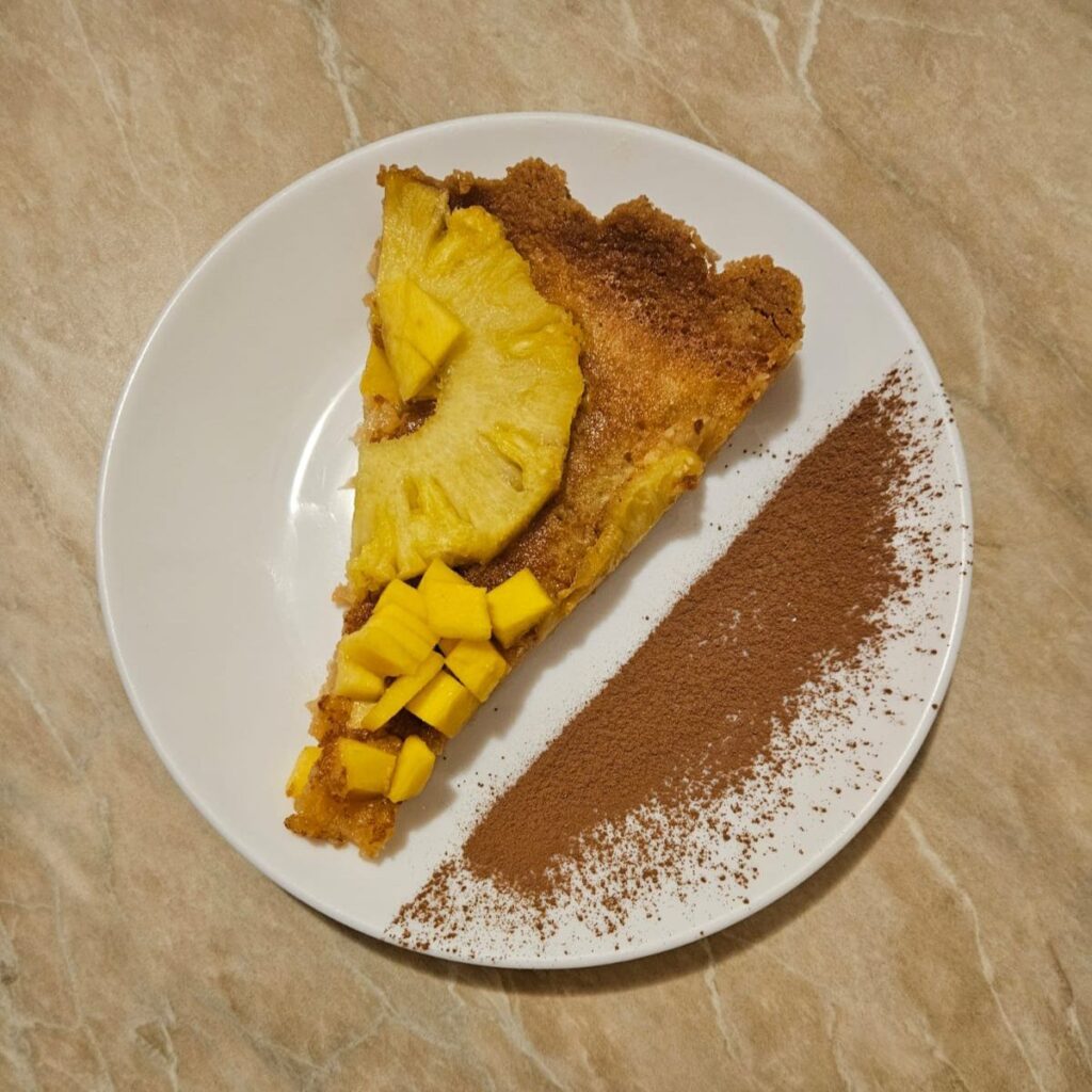 A served slice of Baked Pineapple Mango Tart on a small plate, lightly decorated with cocoa powder.