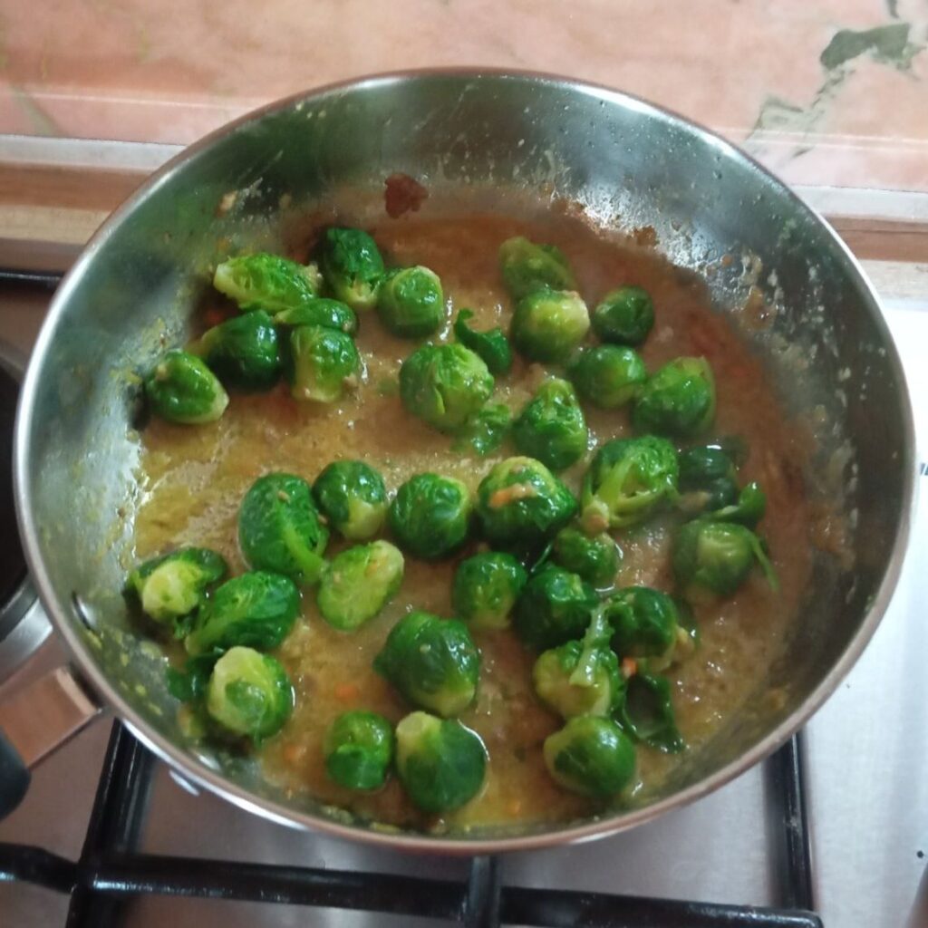 Cooked Brussels sprouts being stirred in the pan to combine with the remaining sauce after the schnitzels are removed.