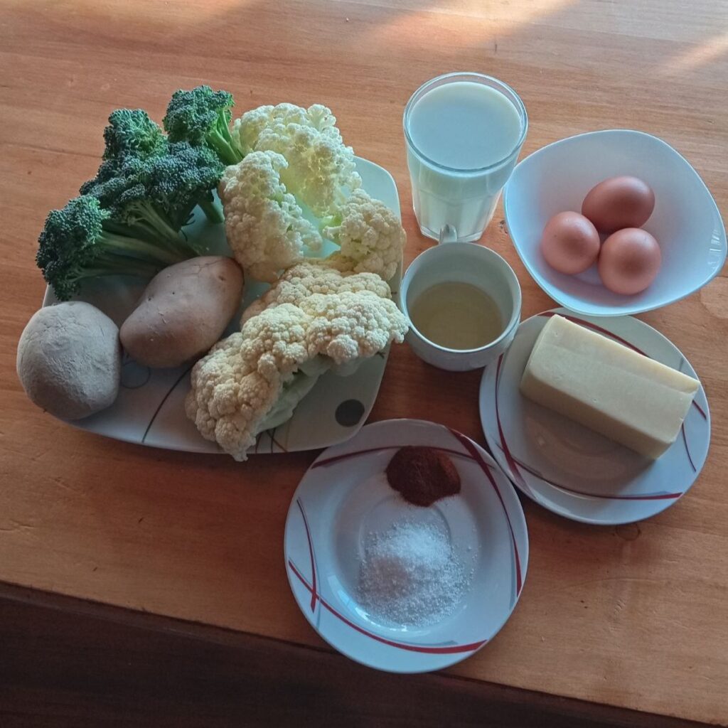 Fresh potatoes, cauliflower, broccoli, eggs, milk, cheese, and seasonings arranged neatly on a table before cooking.