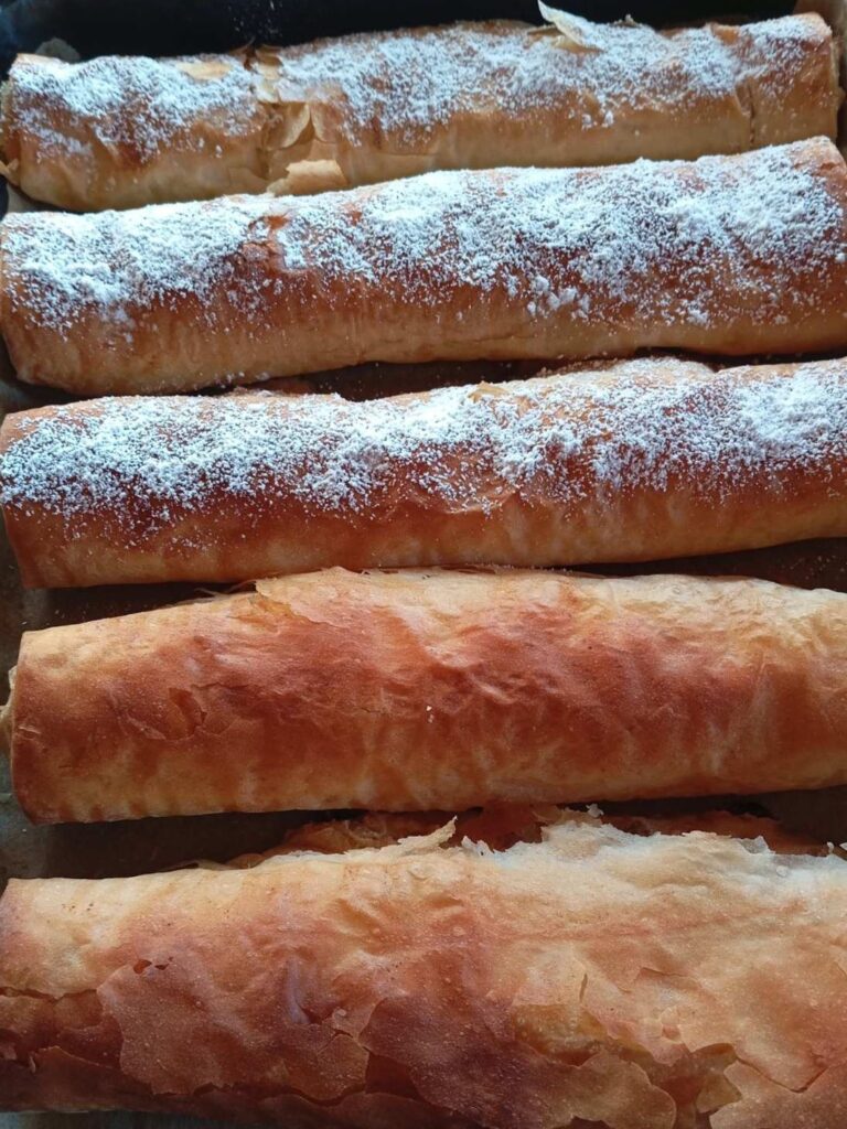 Baked apple raisin phyllo strudels arranged in a baking pan, golden and ready for serving.