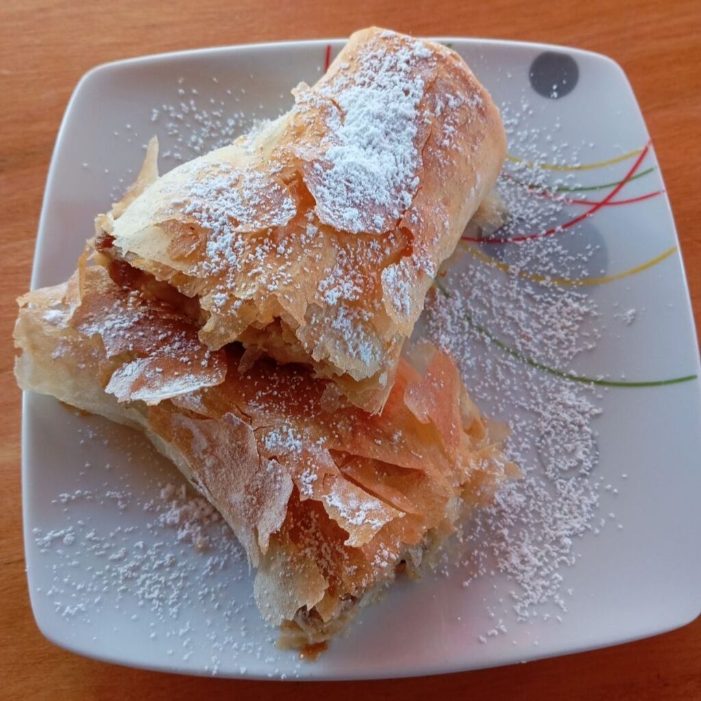 Apple raisin phyllo strudel served on a plate, sliced in half to show the golden phyllo and the apple raisin filling inside.