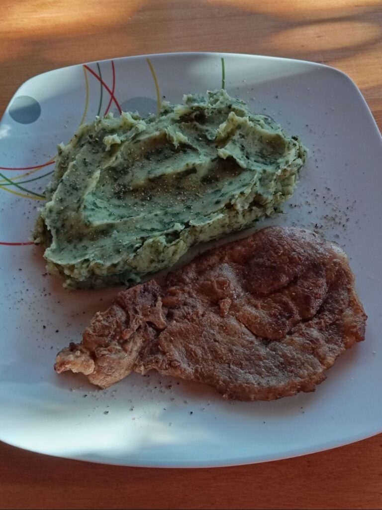 Close-up of a boneless pork neck chop served on a plate with smooth green collard and potato mash.