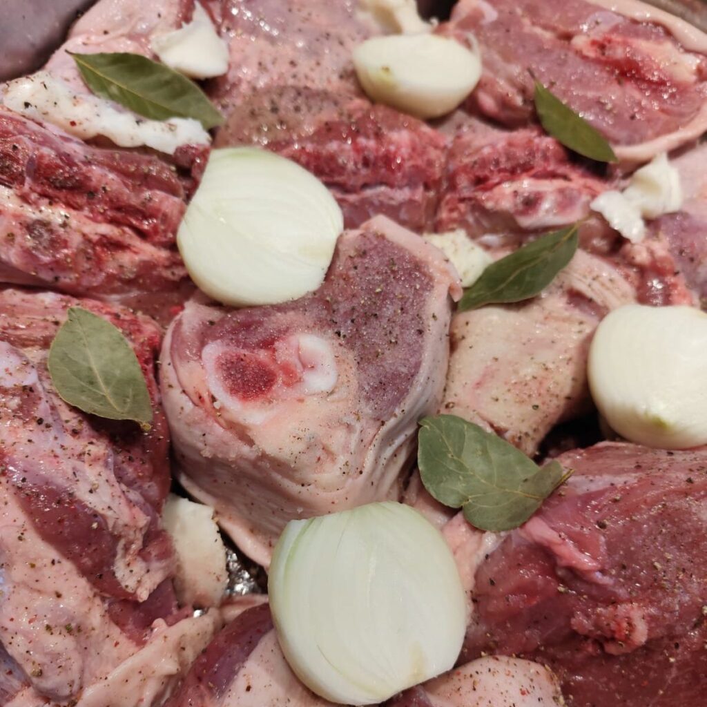 Round pan with meat pieces, pork lard, onions, bay leaves, salt, and pepper.