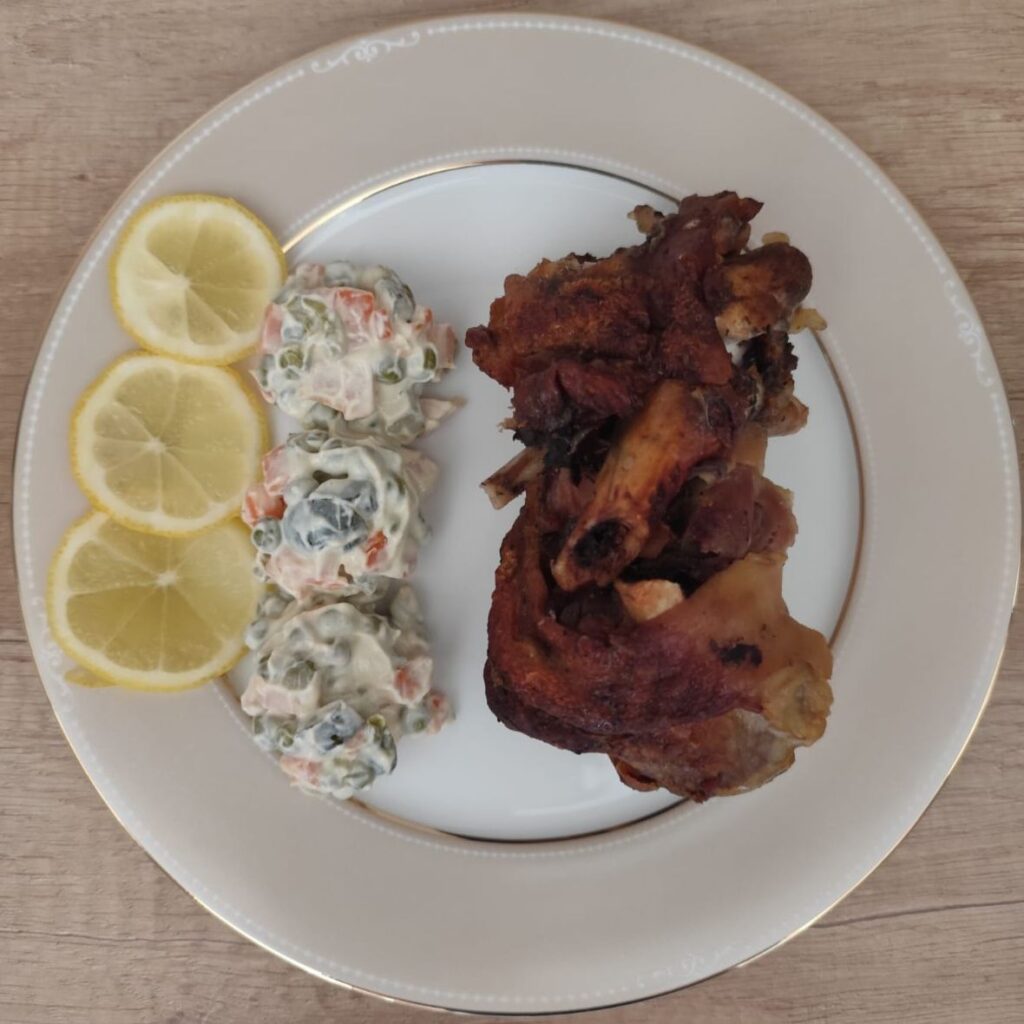 A plated portion of roasted meat served with small scoops of mayonnaise salad on the side.