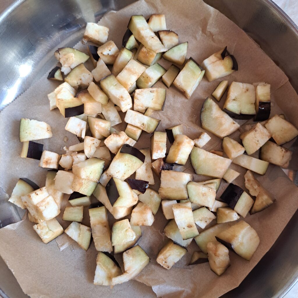 Evenly diced eggplant cubes arranged on baking paper in round tray, prepared for oven baking.