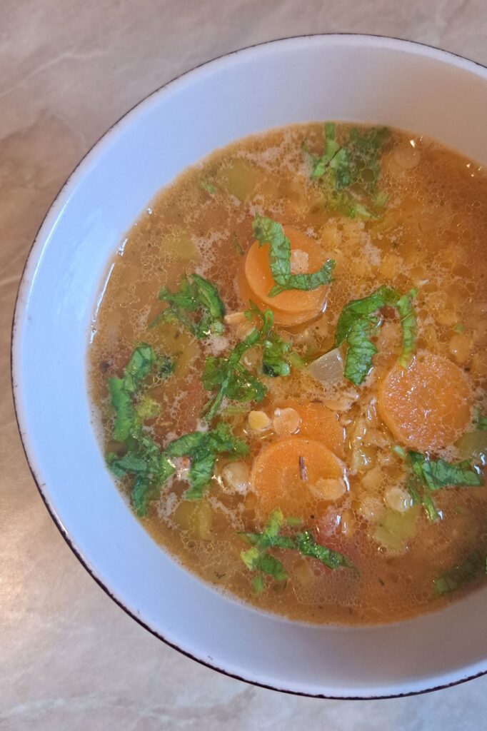 Close-up view of bowl of red lentil soup topped with finely chopped fresh parsley, showing vibrant colors and texture.