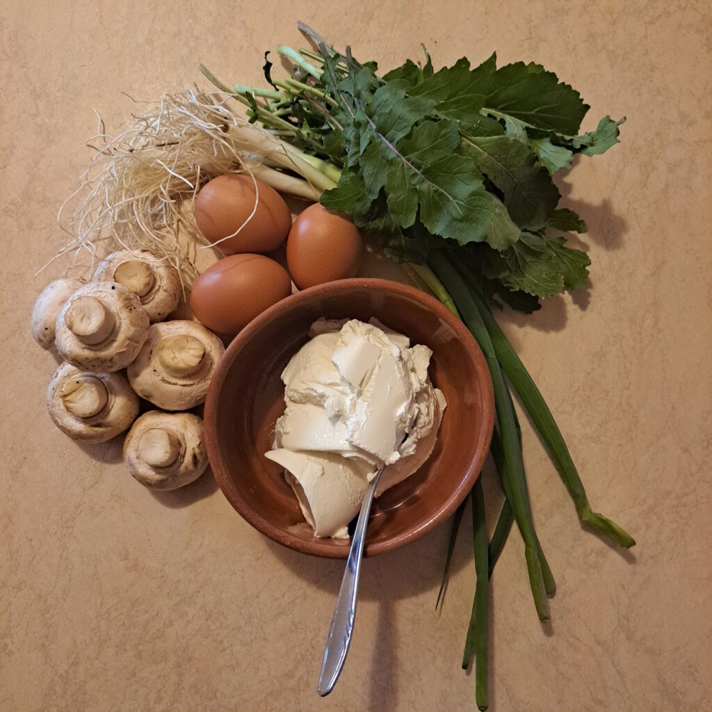 All ingredients for Creamy Mushroom Arugula Omelette neatly arranged on a table, including eggs, mushrooms, arugula, sour cream, and scallion.