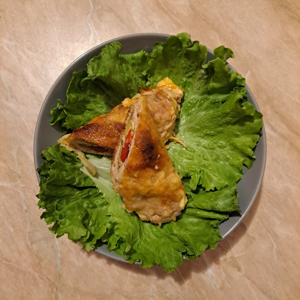 Served Crispy Stuffed Chicken Thighs placed on fresh lettuce leaves on a gray plate, showing a whole baked roll with a golden crust.