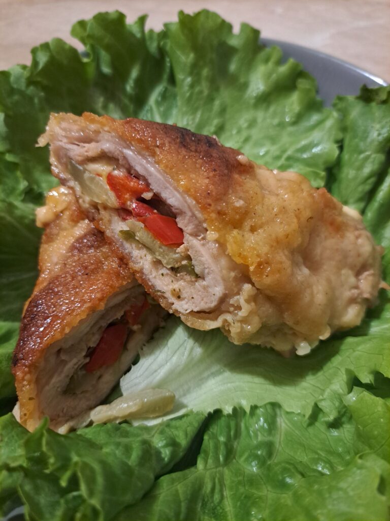 Half-cut crispy stuffed chicken thigh placed on fresh green lettuce leaves on a gray plate, showing melted cheese and colorful vegetables inside.