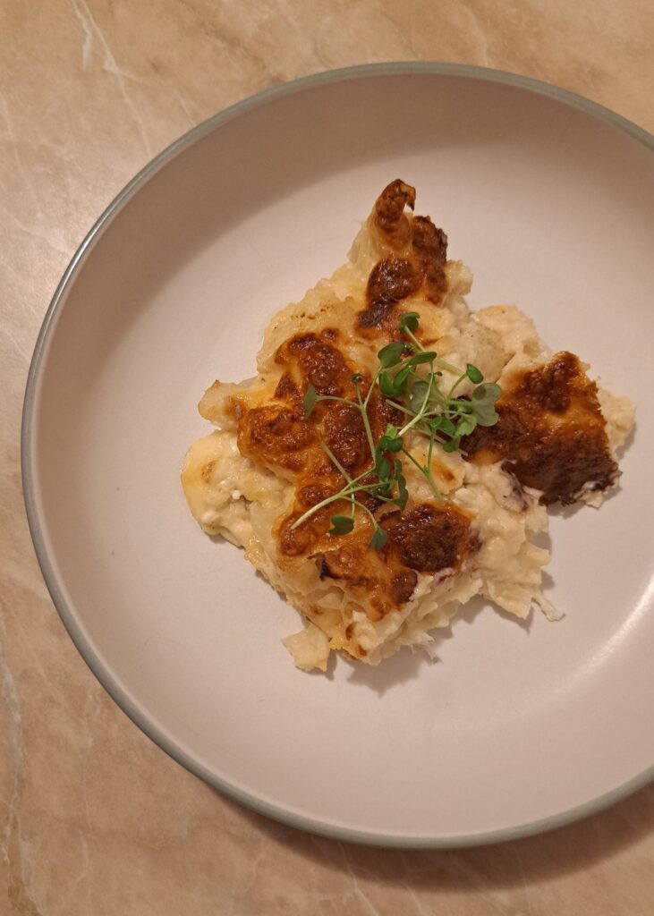 Sliced portion of Creamy Cheesy Cauliflower Bake served on a plate with melted cheese and creamy layers.