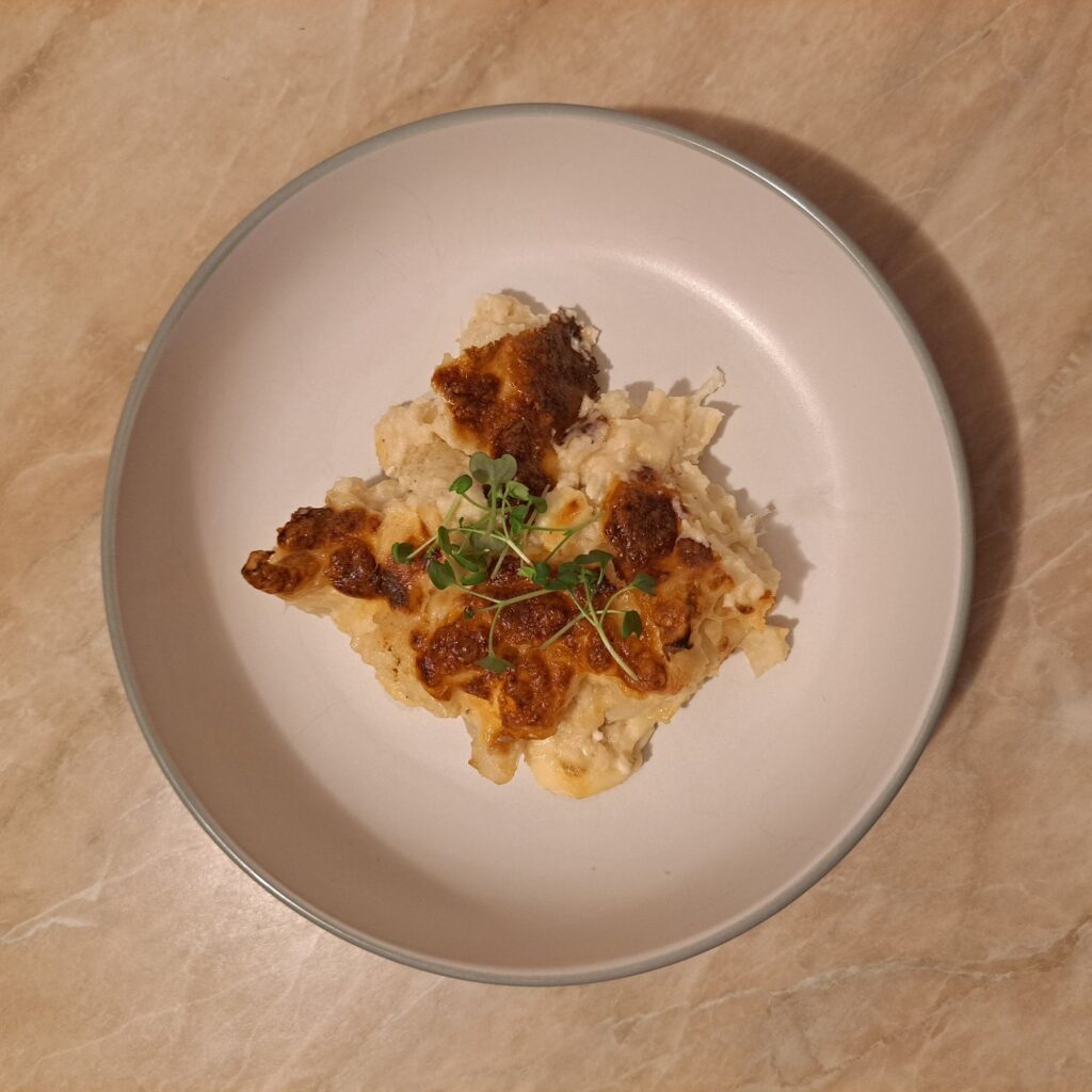 Served slice of Creamy Cheesy Cauliflower Bake on a plate, topped with microgreens and showing creamy cheese layers.