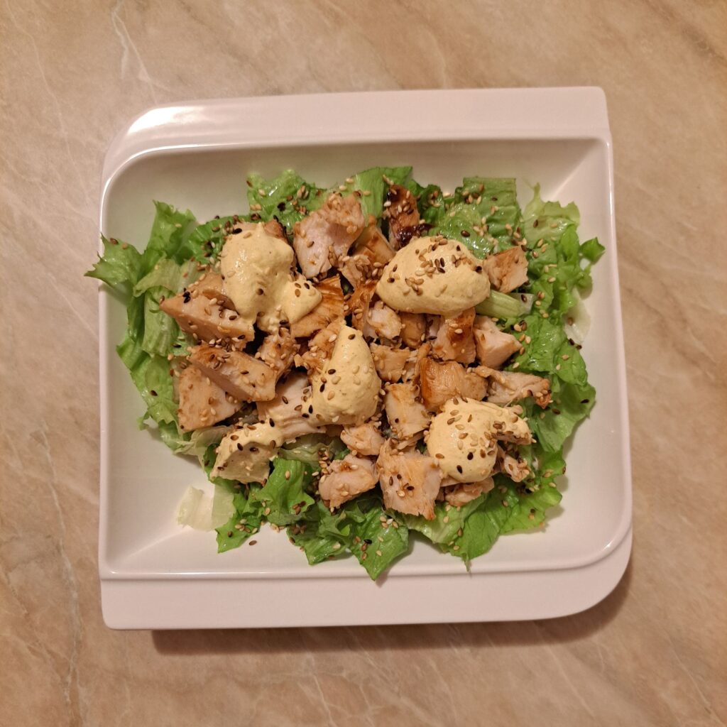 Grilled Chicken Lettuce Salad served on a single plate, showing sliced grilled chicken on fresh chopped lettuce with creamy mustard dressing and toasted sesame sprinkled on top.
