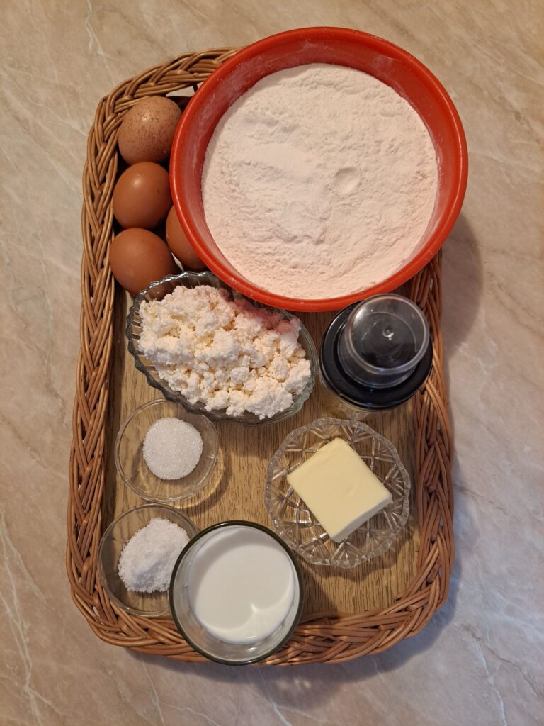 Measured ingredients for Cheese Egg Ring Pie arranged on a flat woven wooden tray, including flour, eggs, cheese, yogurt, oil, butter, salt, and sugar.