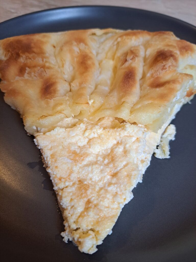 Slice of Cheese Egg Ring Pie served on a black plate, showing golden crust and soft cheese egg filling in the center.