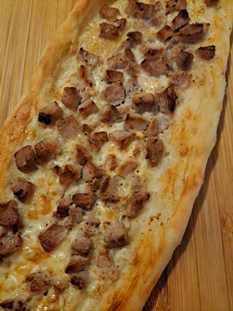 Close-up view of a freshly baked Homemade Cheesy Pork Pastrmajlija showing golden crust, melted cheese, and juicy pork.