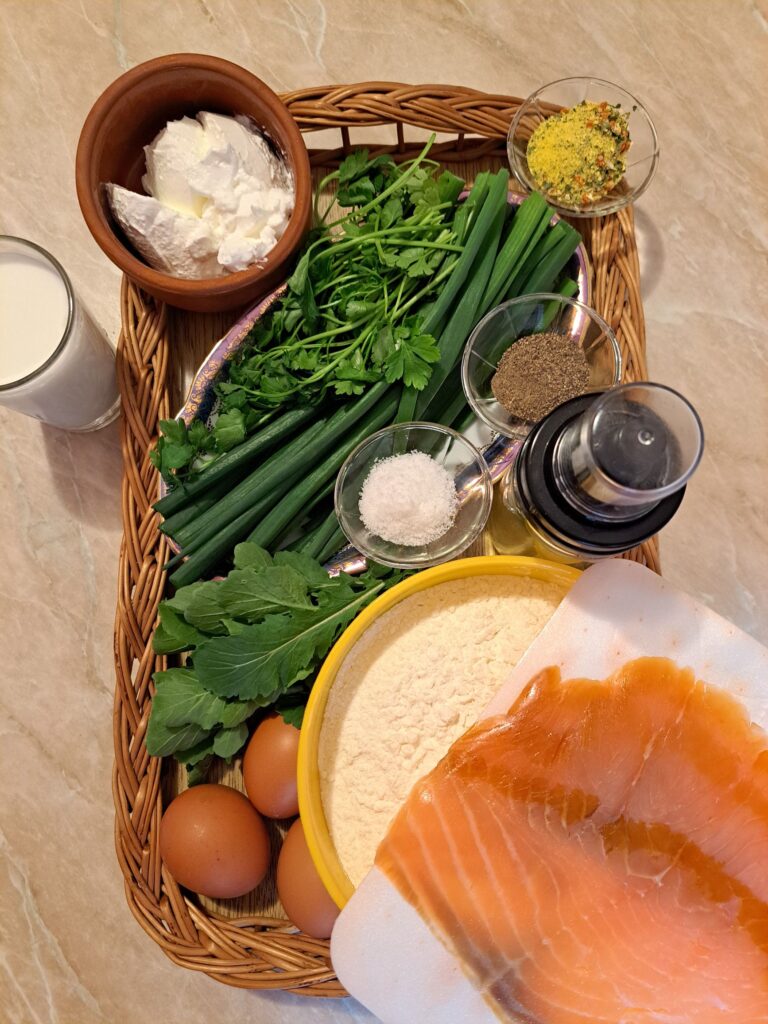All ingredients for smoked salmon savory crepes arranged on a table, including smoked salmon, sour cream, eggs, milk, flour, oil, spices, spring onions, parsley, and arugula.