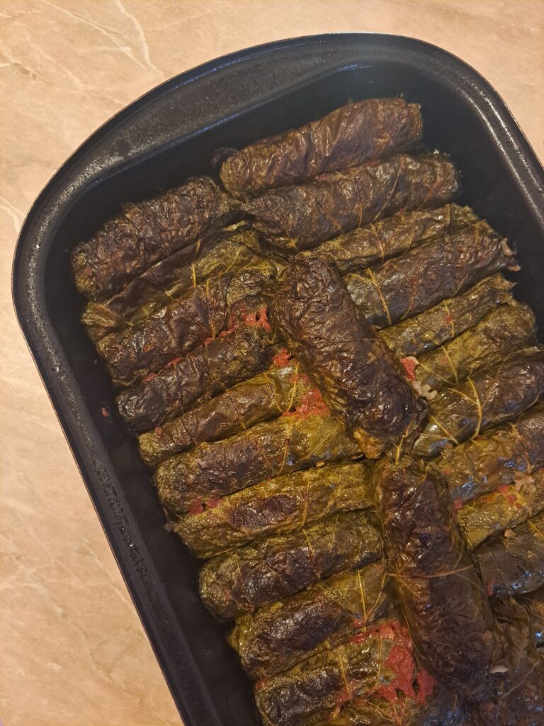 Freshly baked Beef Stuffed Grape Leaves just out of the oven, arranged in a baking tray with dark green grape leaves.