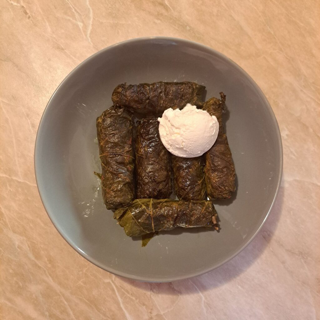Beef Stuffed Grape Leaves served on a gray plate with a scoop of sour cream on the side.