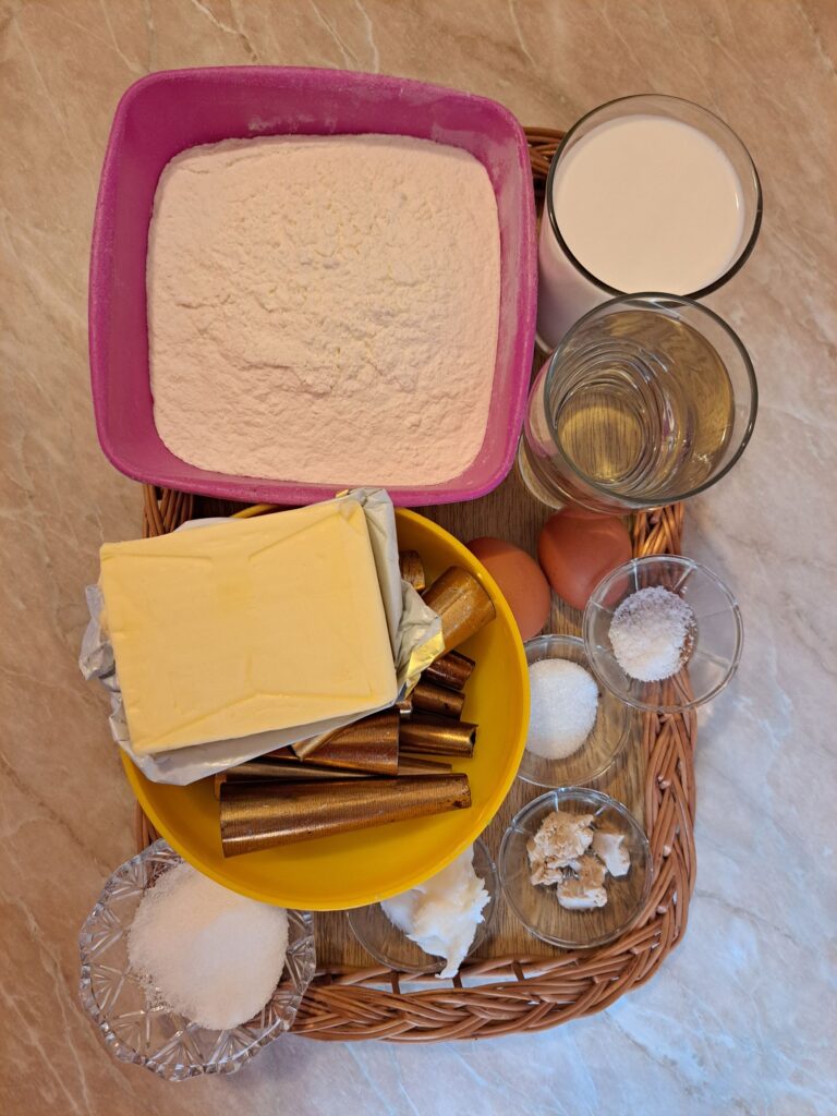 Measured ingredients arranged on a table for Crispy Cream Filled Cones, including flour, milk, eggs, sugar, yeast, butter, and vanilla.