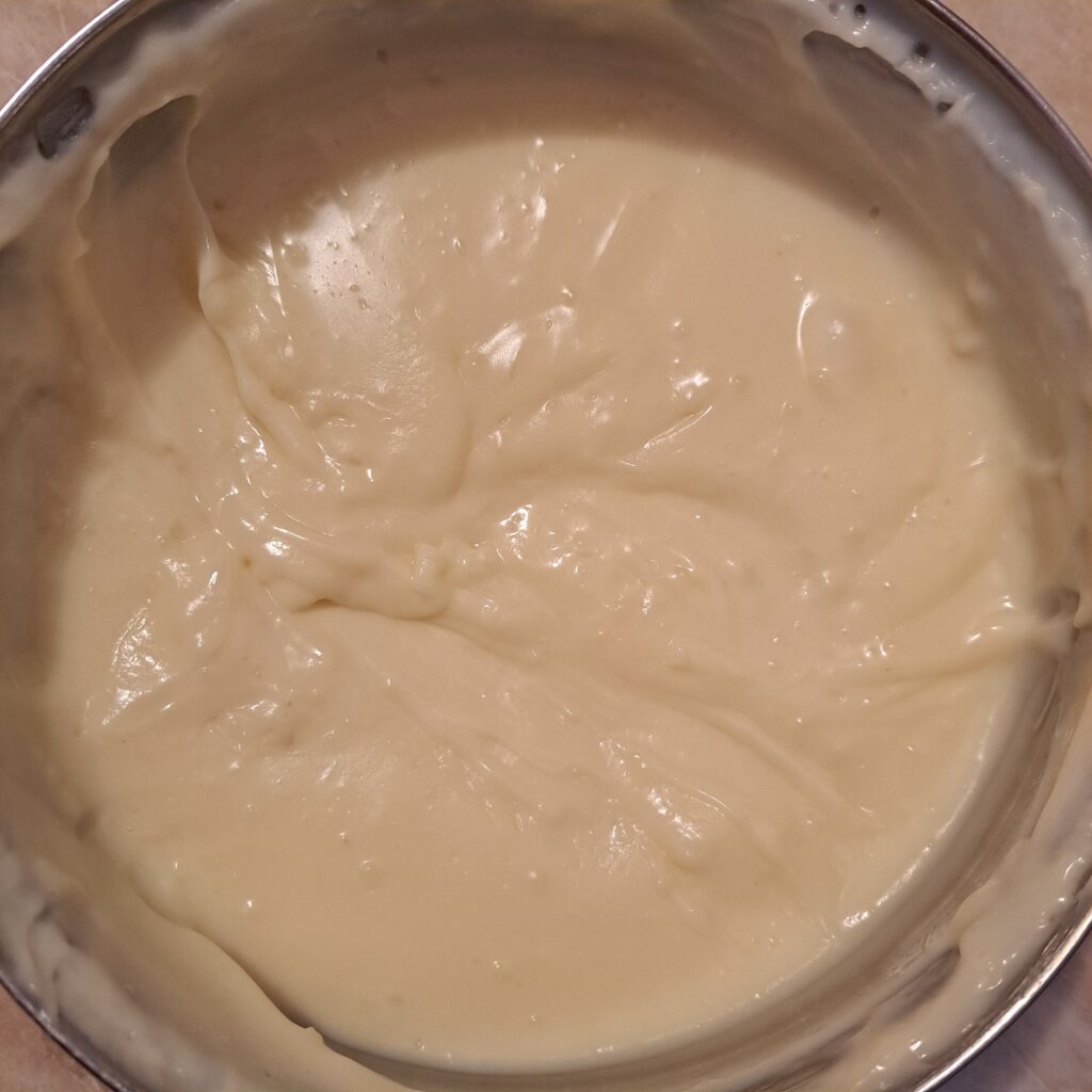 Thick vanilla cream cooking in a deep pot, stirred until smooth and glossy texture forms.