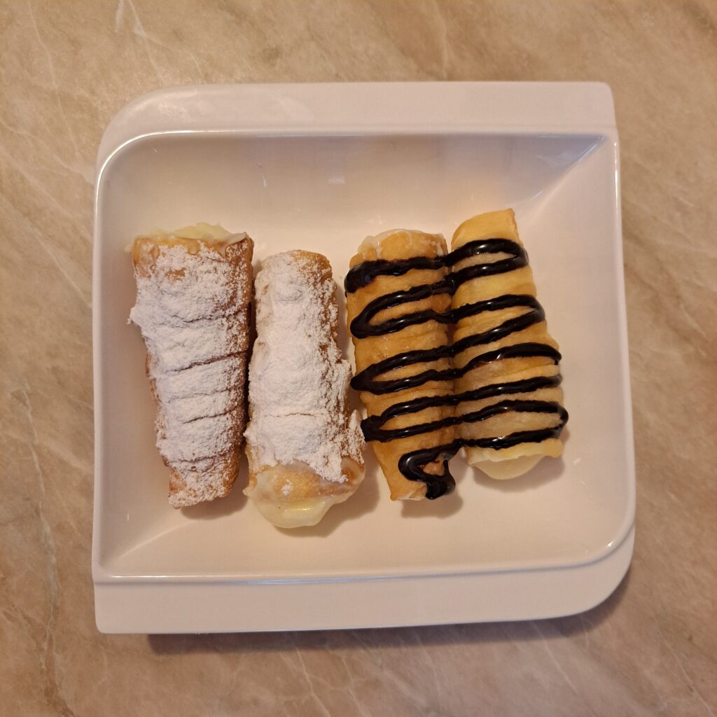 Plate with four Crispy Cream Filled Cones, two dusted with powdered sugar and two topped with chocolate drizzle.