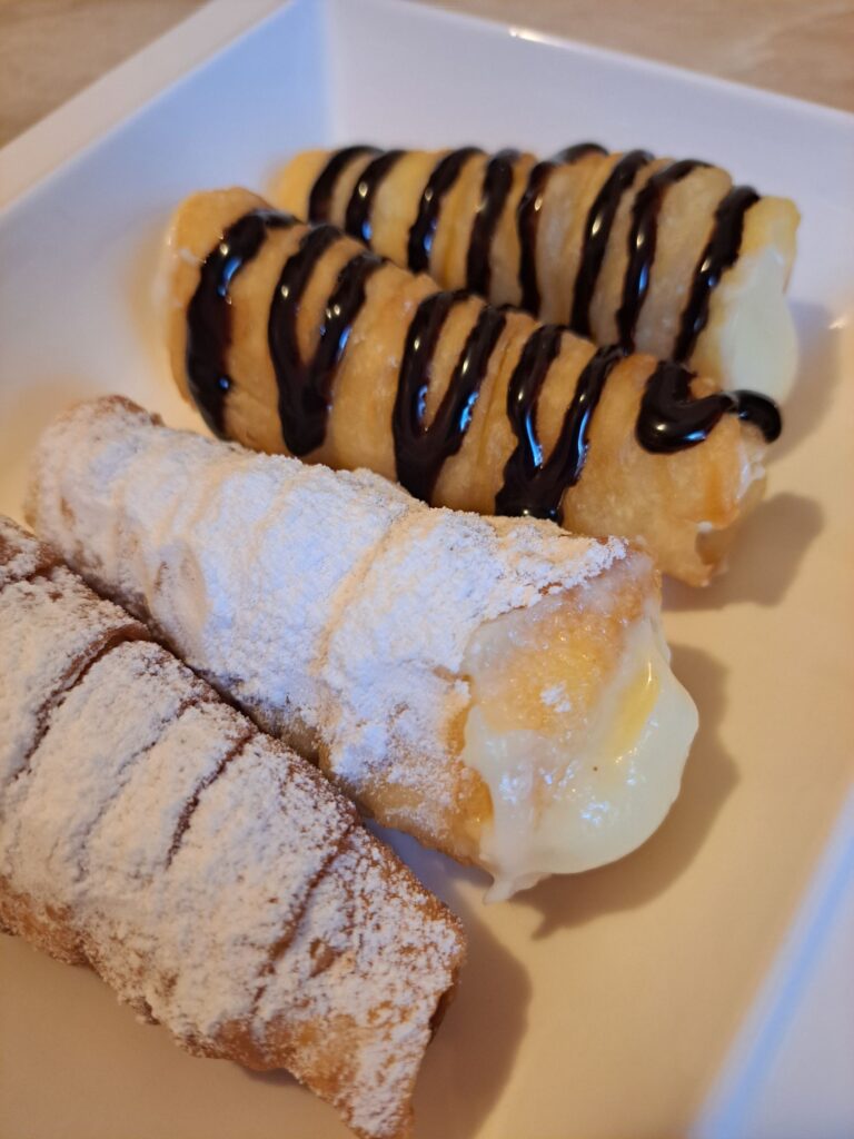 Four Crispy Cream Filled Cones served on a plate, two dusted with powdered sugar and two topped with chocolate drizzle.