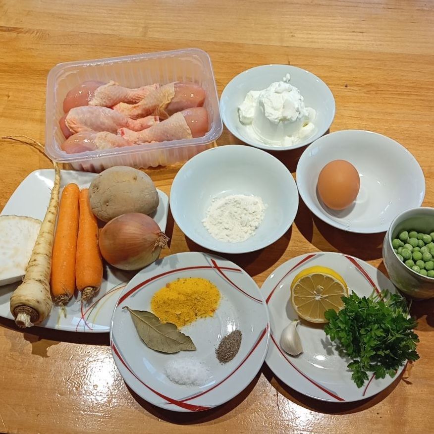 All ingredients for Creamy White Chicken Soup arranged on a table, including chicken, vegetables, egg, flour, sour cream, lemon, and seasonings, ready for preparation.