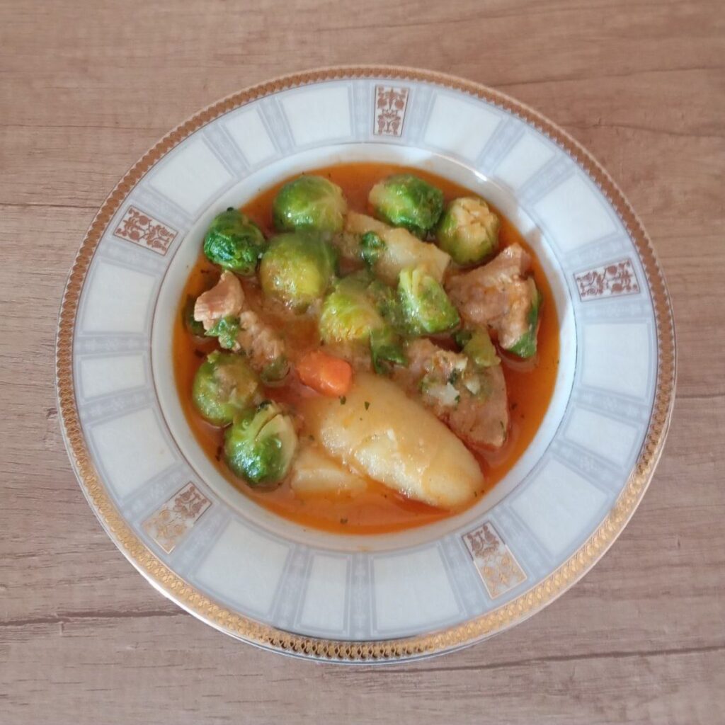 Wide deep bowl filled with Pork Potato Brussels Stew, showing chunks of pork, potatoes, and Brussels sprouts.