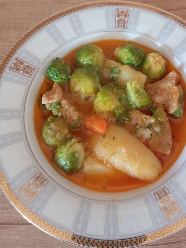 Wide deep bowl with Pork Potato Brussels Stew, showing chunks of pork, potatoes, and Brussels sprouts.