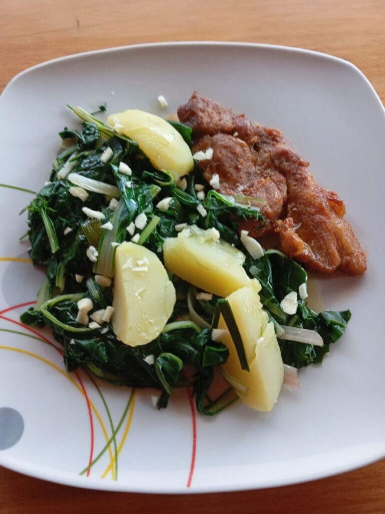 Close-up of pork chops served with boiled potatoes and chard on a rustic dinner plate with olive oil and garlic.