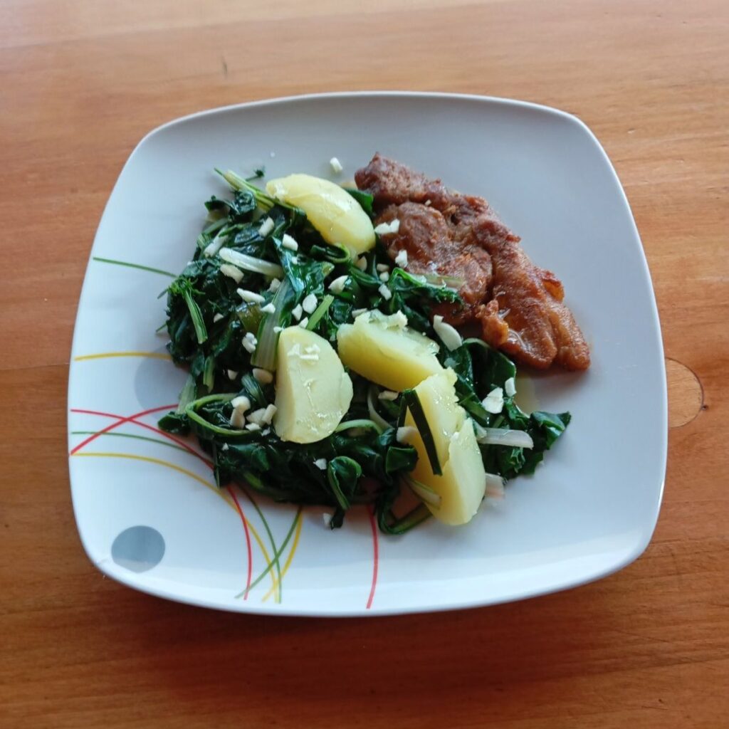 Served plate of Pork Chops Potato Chard with boiled potatoes, chard, and a golden fried pork chop finished with olive oil and garlic.