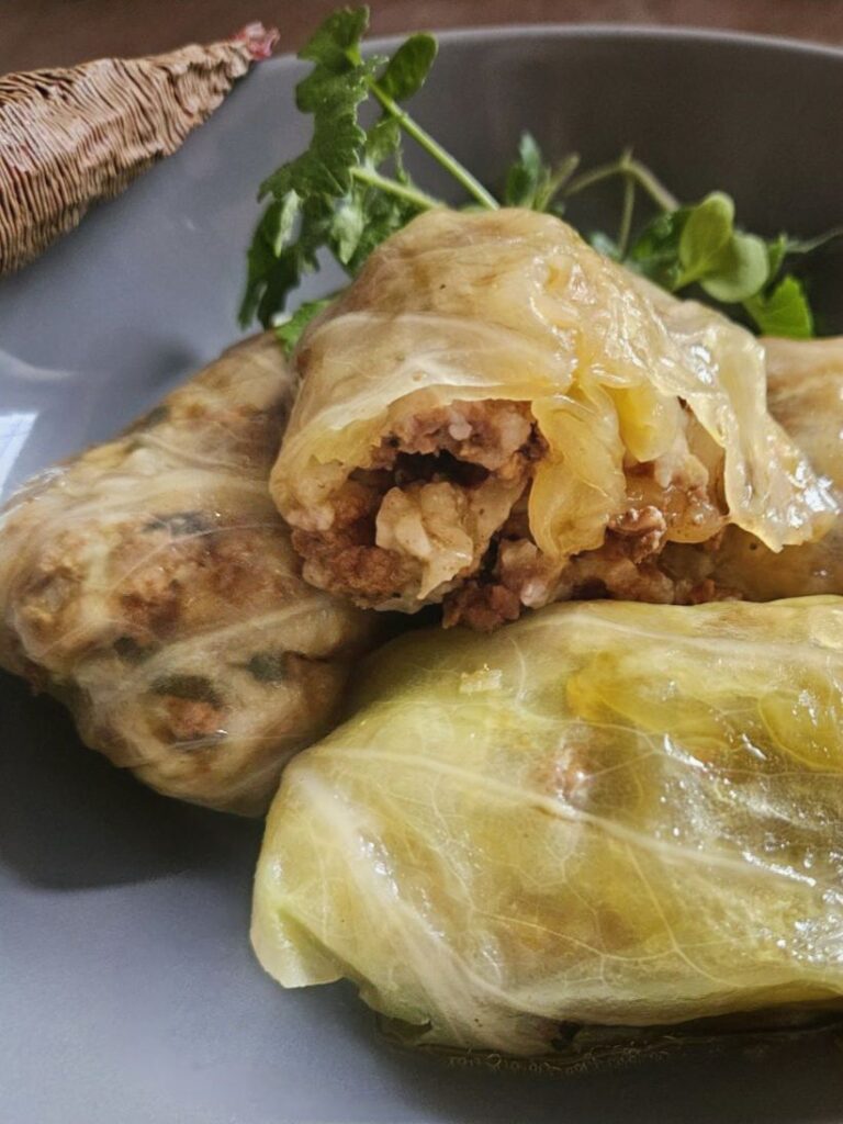 Three stuffed fermented cabbage rolls served in a deep plate, shown close up.