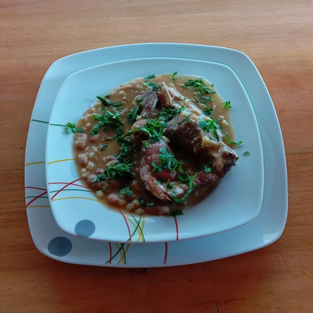 Bean Soup with Smoked Mutton served in a deep plate with visible beans, barley, vegetables, and pieces of smoked mutton, topped with chopped parsley.