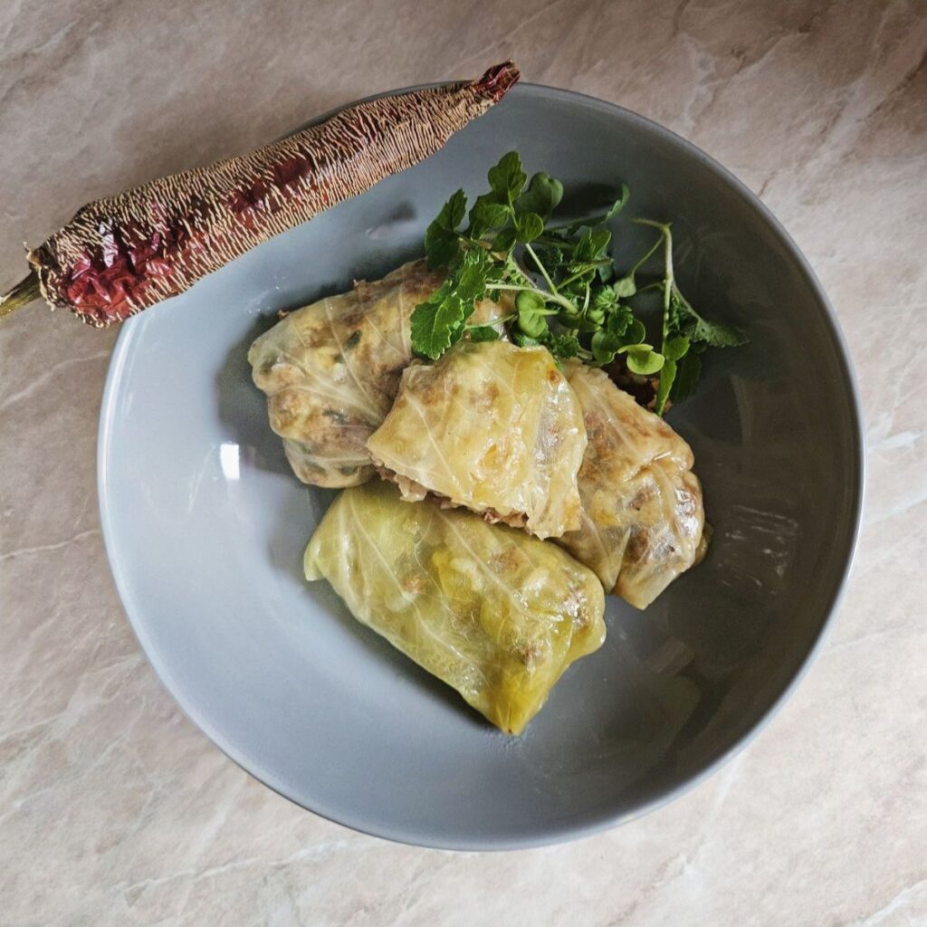 Stuffed Fermented Cabbage Rolls served in a plate with microgreens and a whole dried red pepper.
