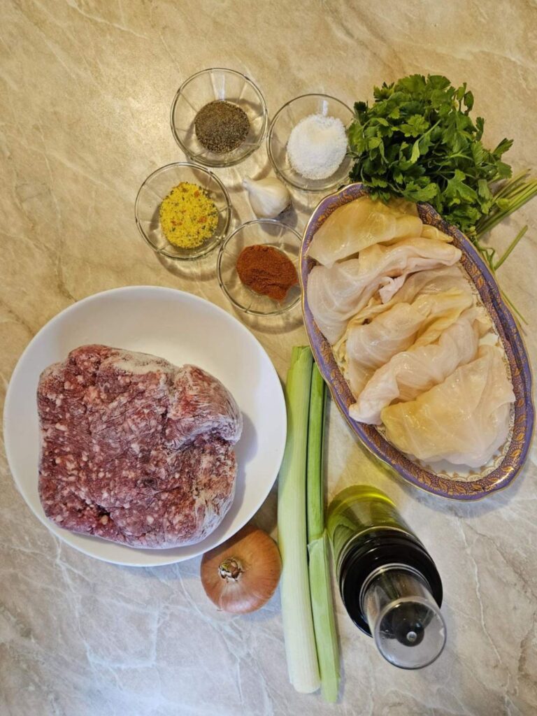 Fermented cabbage leaves, mixed pork and beef, rice, onion, leek, garlic, parsley, and spices arranged on a table.