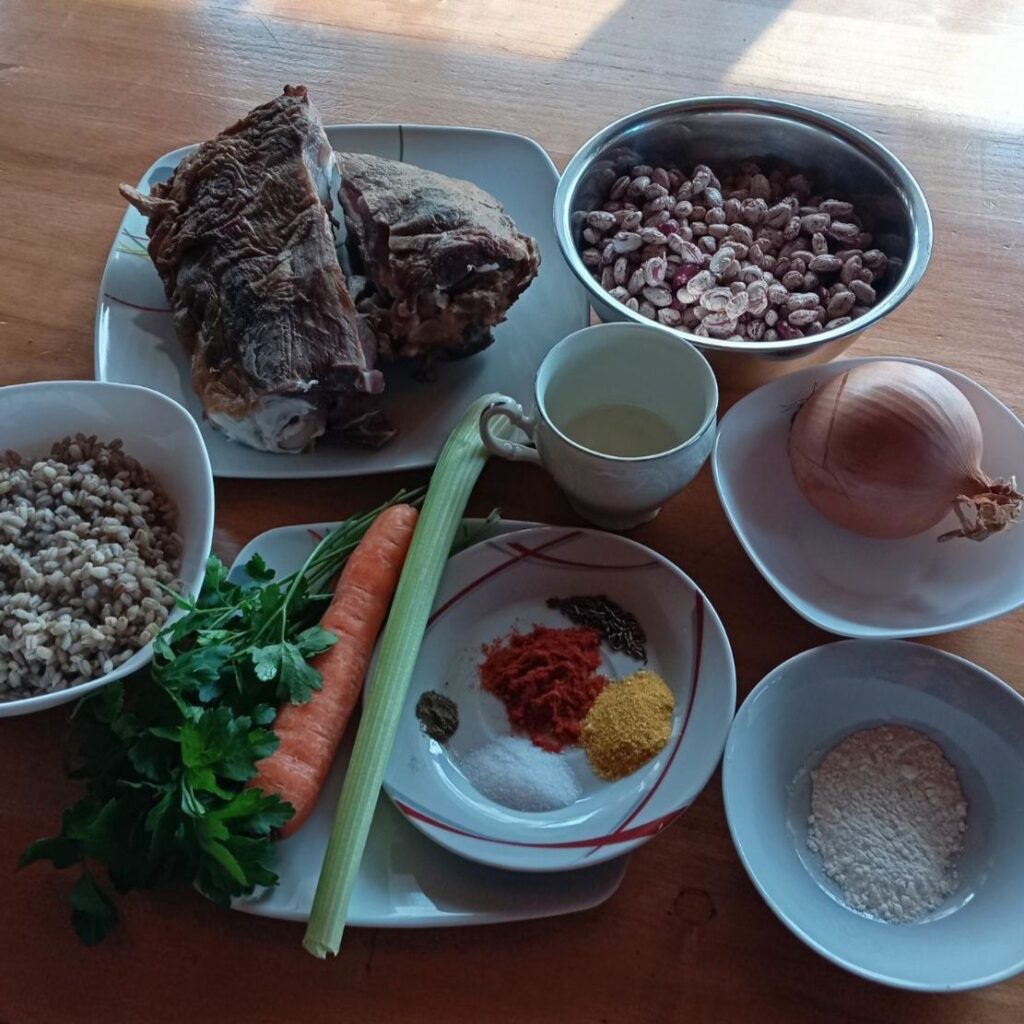Ingredients for bean soup with smoked mutton arranged on a surface, including beans, smoked mutton, barley, vegetables, spices, and parsley.