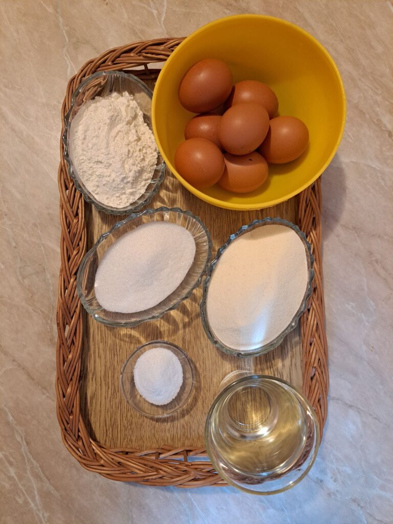 Measured ingredients for sweet syrup semolina cake including eggs, sugar, semolina, flour, water, and vanilla sugar arranged on a kitchen surface.