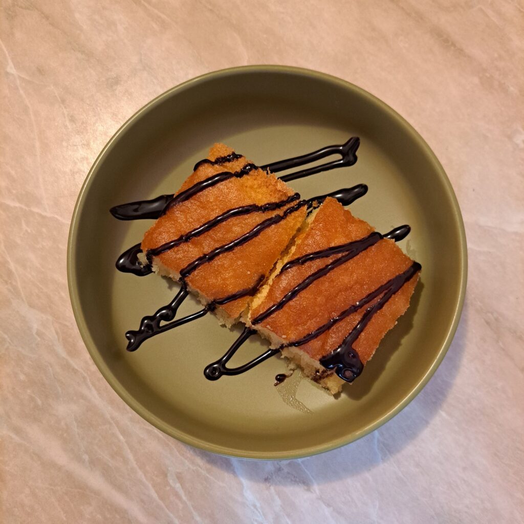 Sweet Syrup Semolina Cake served as two neat cubes on a small plate, lightly drizzled with chocolate and ready to enjoy.