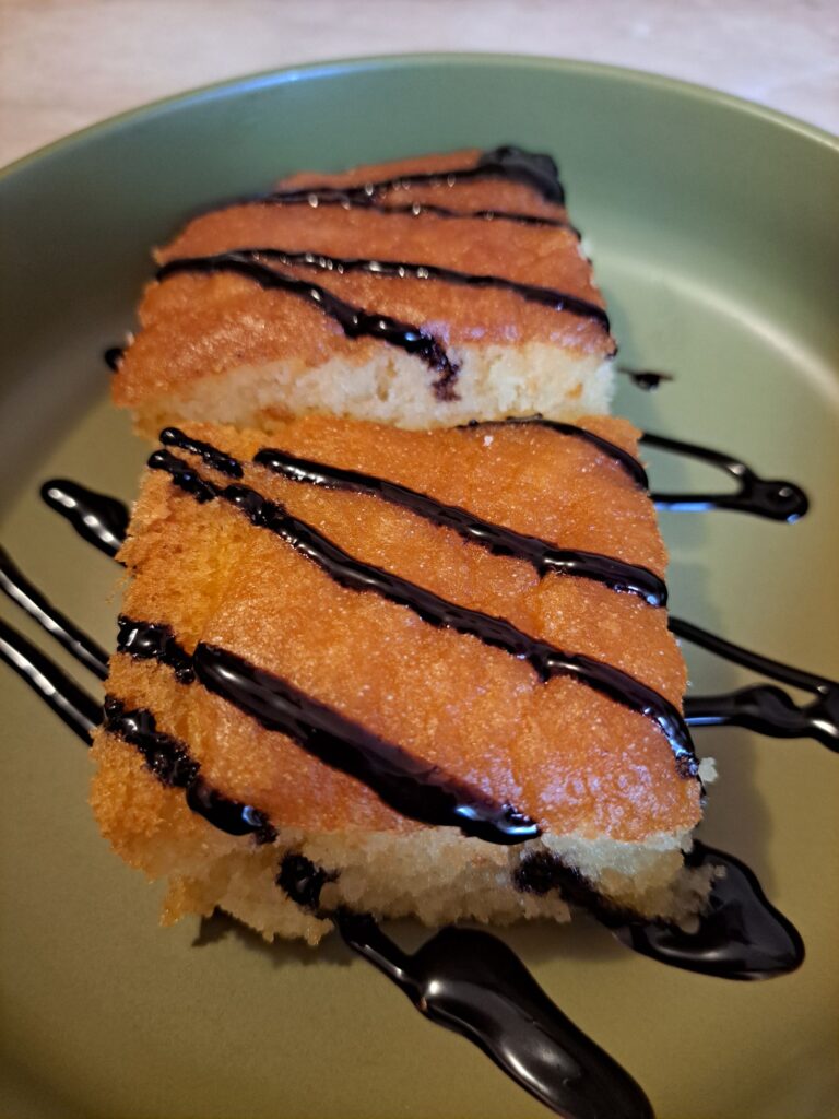 Two pieces of sweet syrup semolina cake served on a small round green plate, lightly drizzled with chocolate and neatly presented.