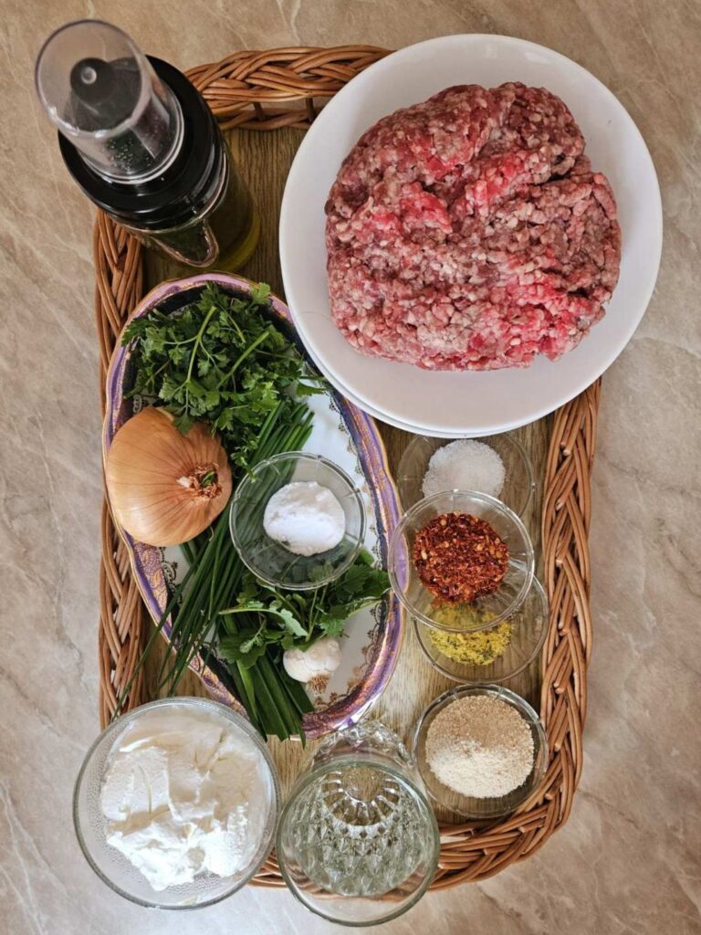 All ingredients for creamy white sauce meatballs arranged on a wooden board, including ground meat, onion, garlic, parsley, breadcrumbs, cream, and spices neatly displayed.
