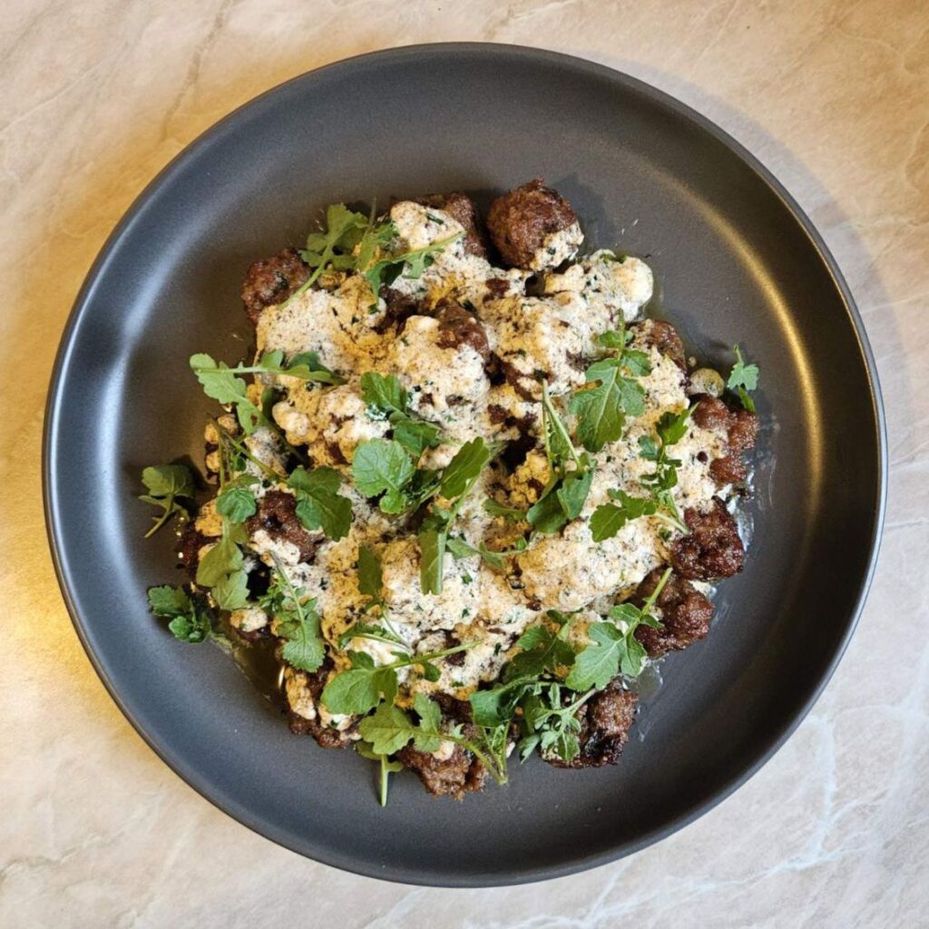 Creamy White Sauce Meatballs served on a flat black plate, topped with smooth white sauce and garnished with fresh arugula microgreens.